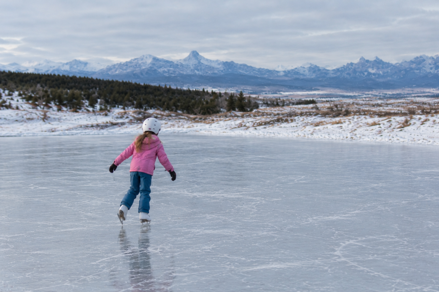 A young skater gliding across the ice with snowy mountains beyond